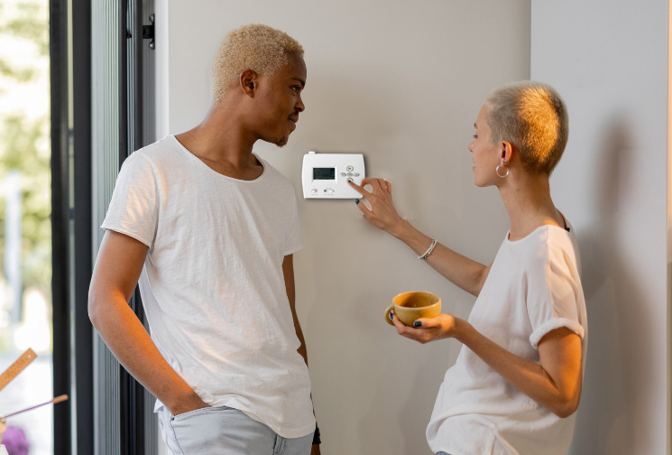 Man and woman in white t-shirts adjusting a wall thermostat