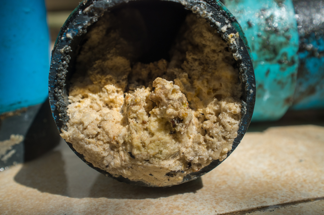 Piece of kitchen pipe full of grease laying on tile floor.