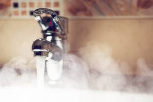 Bathroom faucet running hot water and steam rising from sink.