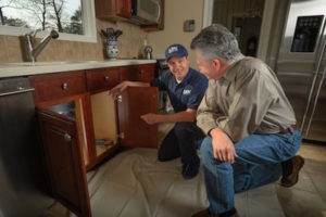 Len the Plumber technician and homeowner in the DC Metro area kneeling and talking in front of sink.