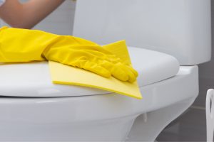 Gloved hand cleaning toilet lid