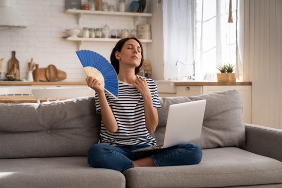 Woman sitting on couch with a blue fan and laptop